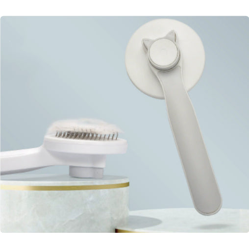 Gray self-cleaning pet grooming brush shown from the rear and pin-face side.