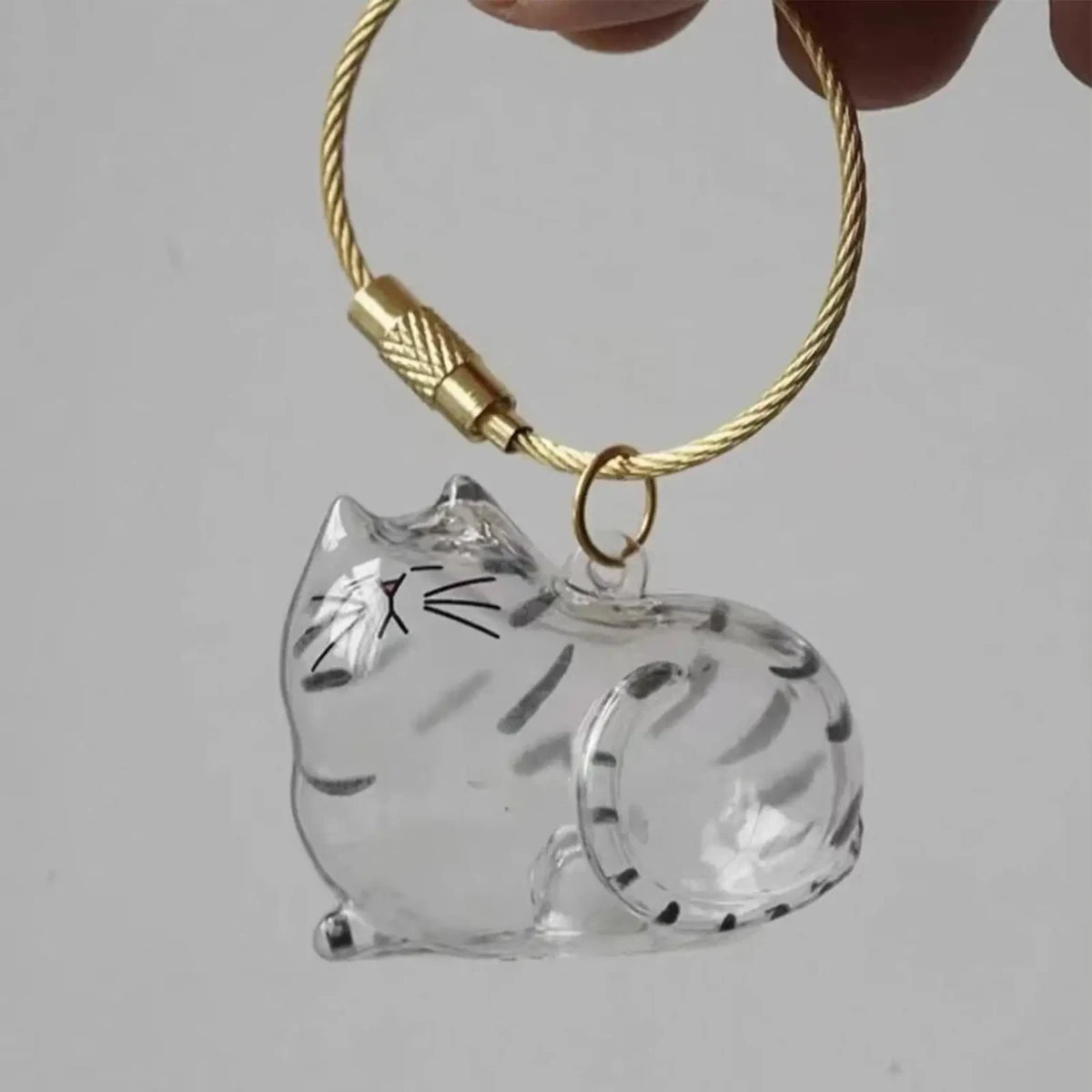 Empty Silver Tabby cat-shaped keepsake keychain held in one hand, showing the clear compartment and loop.