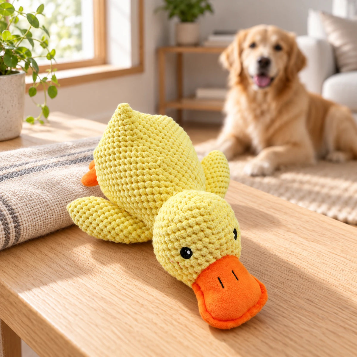Yellow plush squeaky duck toy with an orange beak on a light wood surface, with a dog in the background.