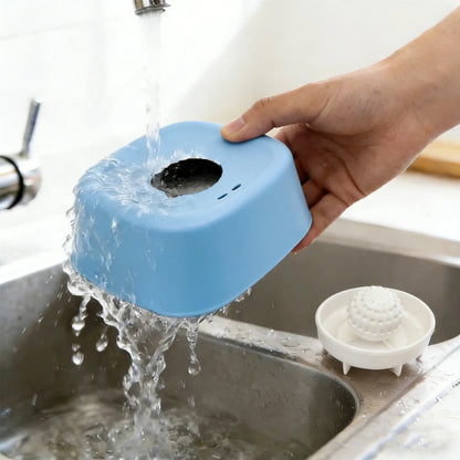 Blue rolling lick bowl being rinsed under a faucet, with its white insert beside it.