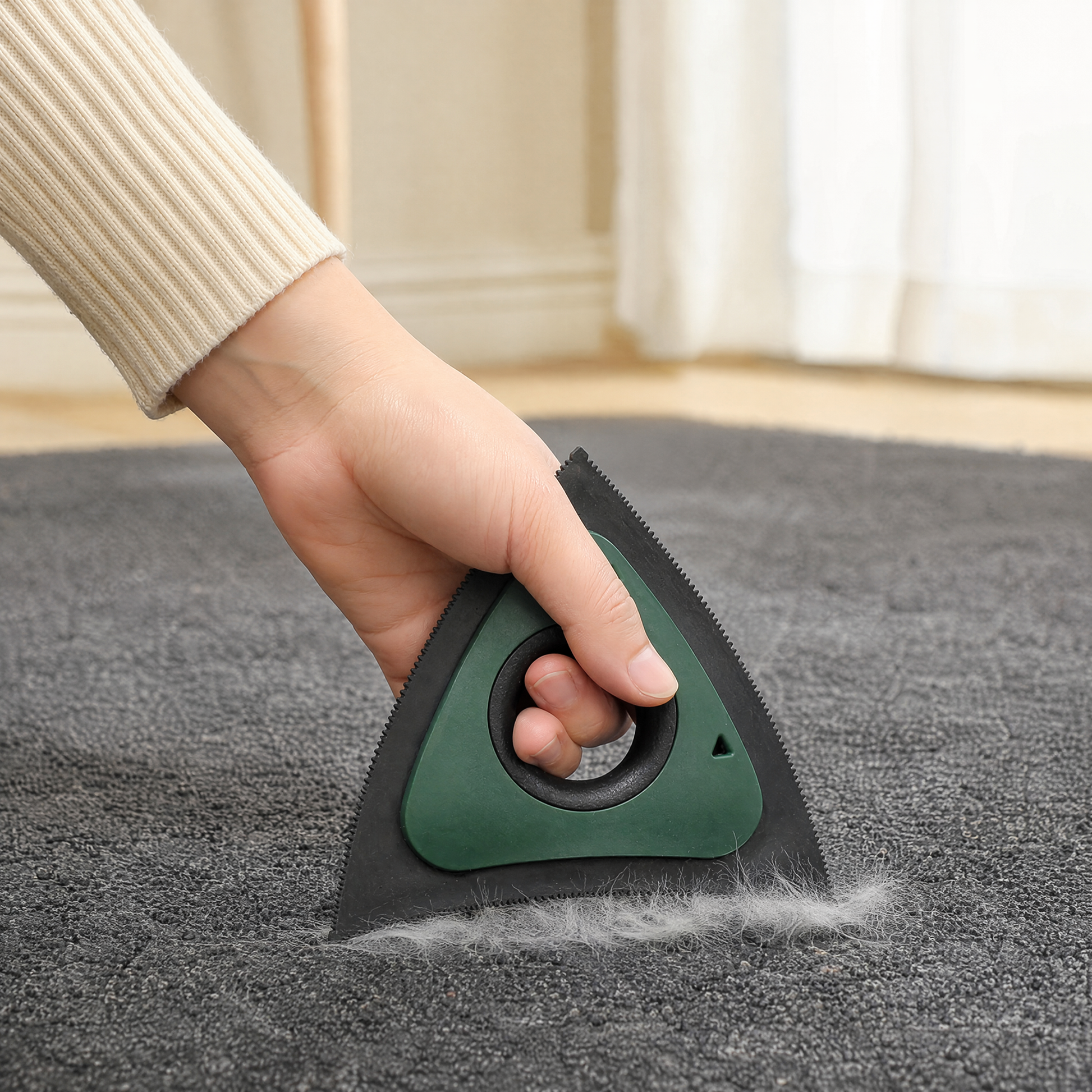 Hand using a green tri-edge pet hair scraper to gather loose hair from a carpet